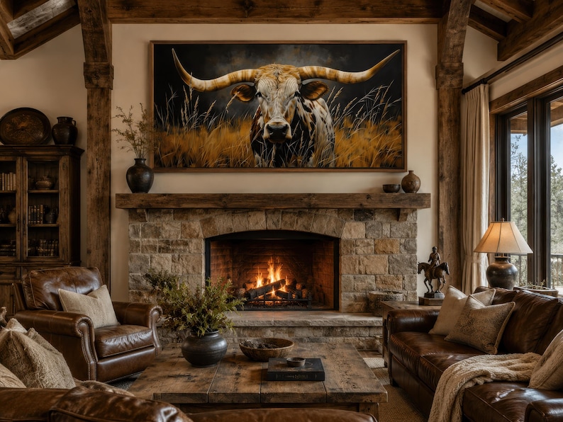 May include: A cozy living room with a stone fireplace and a large framed painting of a longhorn. The room features leather furniture, a wooden coffee table, and a warm, inviting atmosphere. The fireplace has a burning fire.