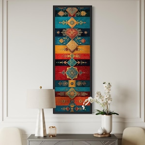 May include: A framed vertical artwork with a colorful, geometric design. The artwork features alternating bands of teal, red, yellow, and black, each adorned with intricate, gold-colored patterns. The piece is displayed above a gray cabinet with a lamp and vase.