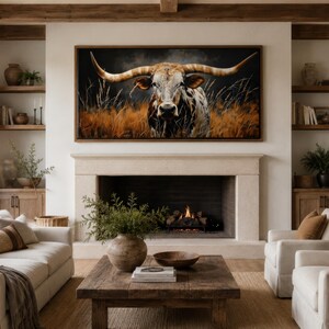 May include: A living room with a large framed canvas featuring a longhorn in a field. The room has a fireplace, two white sofas, two white armchairs, and a wooden coffee table. The room is decorated in neutral tones with wooden accents.