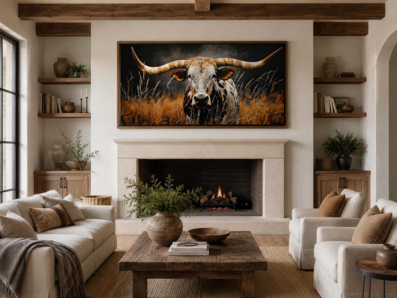 May include: A living room with a large framed canvas featuring a longhorn in a field. The room has a fireplace, two white sofas, two white armchairs, and a wooden coffee table. The room is decorated in neutral tones with wooden accents.