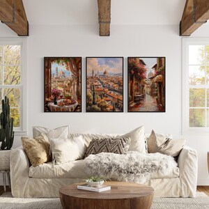 a cozy living room with a large window overlooking a picturesque cityscape. The room is decorated with a plush white sofa, a wooden coffee table, and various potted plants. Three framed pictures are hung on the wall, depicting a city scene with a bridge and a canal.