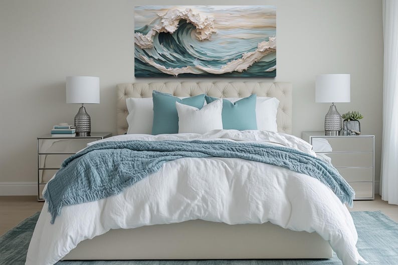 a serene and inviting bedroom with a large bed adorned with a white comforter and a blue throw blanket. The bed is flanked by two nightstands, each with a lamp, creating a cozy and well-lit atmosphere. Above the bed, a large painting of a crashing wave adds a touch of nature and artistic flair to the room.