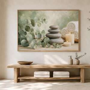May include: A rectangular wall art print featuring a stack of smooth grey stones, green eucalyptus branches, rolled white towels, and two lit cream-coloured candles against a soft, muted green and beige watercolour-style background.