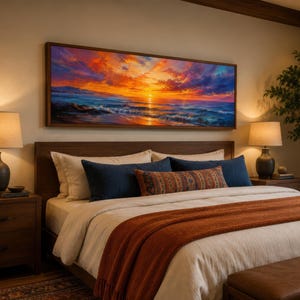 May include: A rectangular wall art print featuring a vibrant sunset over the ocean with orange, yellow, and purple clouds above deep blue waves. The artwork is displayed in a wooden frame above a bed with white bedding and a rust-coloured throw.
