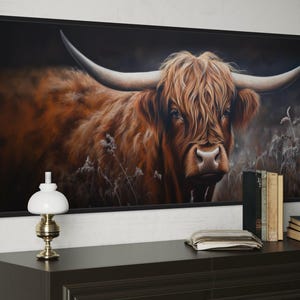 a large framed painting of a horned animal, likely a yak or a bull, with a dark background and a lighter background. The painting is hanging on a wall above a wooden dresser, which has a lamp, a stack of books, and a clock on it.