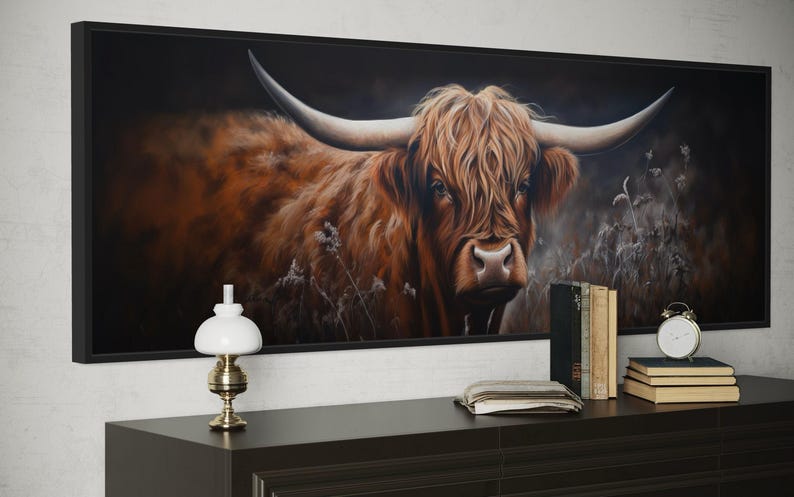 a large framed painting of a horned animal, likely a yak or a bull, with a dark background and a lighter background. The painting is hanging on a wall above a wooden dresser, which has a lamp, a stack of books, and a clock on it.