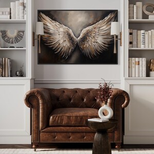 a living room with a brown leather armchair, a wooden side table, and a large framed artwork of a pair of angel wings hanging on the wall above the armchair.