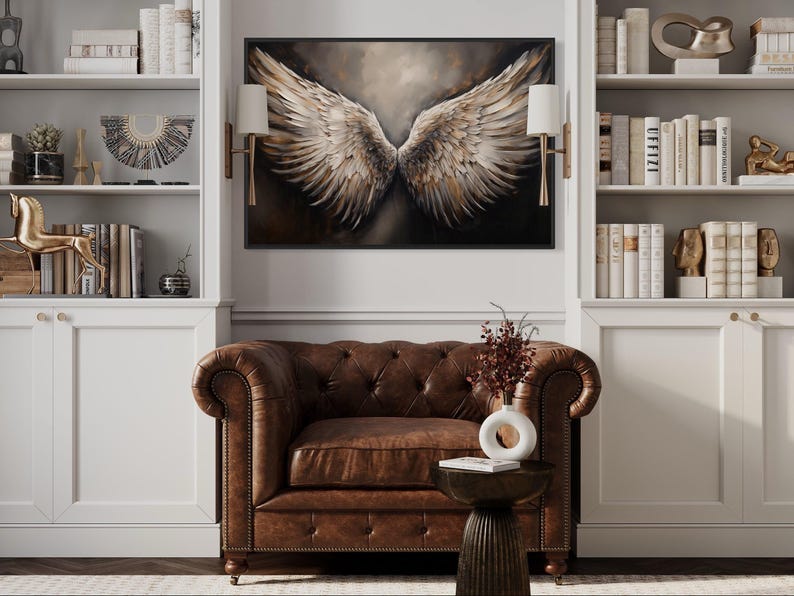 a living room with a brown leather armchair, a wooden side table, and a large framed artwork of a pair of angel wings hanging on the wall above the armchair.