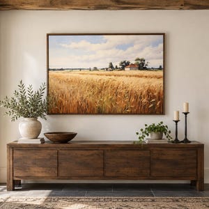 May include: A rectangular landscape painting featuring a golden wheat field under a blue sky with white clouds, displayed in a thin brown frame above a long, dark wooden console table with four cabinet doors and a smooth, flat top surface.