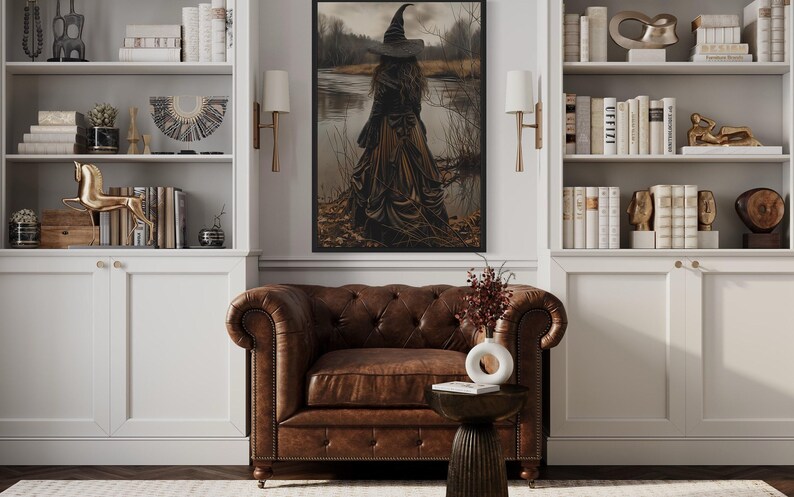 a cozy living room with a brown leather armchair, a wooden side table, and a bookshelf filled with books and decorative items. A large painting of a woman in a long black dress is hanging on the wall above the armchair, and a vase of flowers is placed on the side table.