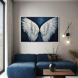 a modern living room with a large blue sofa, a wooden coffee table, and a framed artwork of white wings hanging on the wall above the sofa.