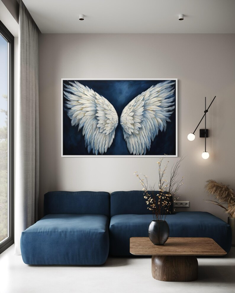 a modern living room with a large blue sofa, a wooden coffee table, and a framed artwork of white wings hanging on the wall above the sofa.