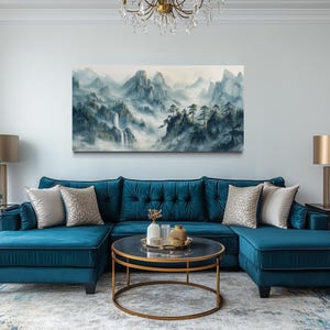 a living room with a large blue sectional sofa, a round coffee table, and a painting of a mountainous landscape hanging on the wall above the sofa.