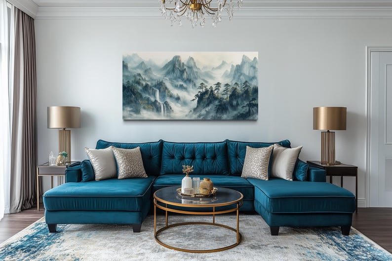 a living room with a large blue sectional sofa, a round coffee table, and a painting of a mountainous landscape hanging on the wall above the sofa.