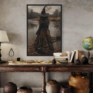 a dark-themed room with a large framed picture of a witch standing in a field, a wooden table with various knick-knacks, and a globe on top.