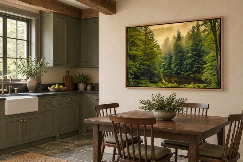 May include: A large rectangular framed wall art piece depicting a dense, misty forest with tall green pine trees and golden light. The artwork is mounted on a light-colored wall above a wooden dining table with chairs in a kitchen.