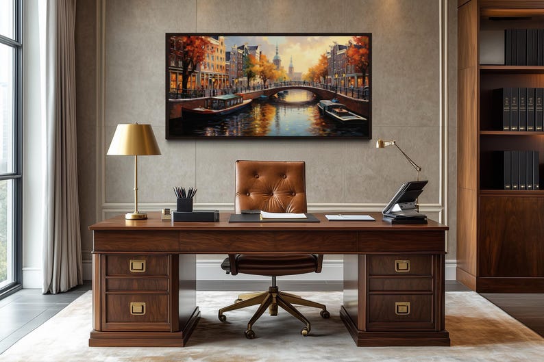 a large wooden desk with a leather chair, a lamp, and a framed painting of a canal scene above it.