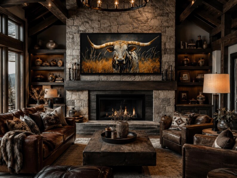 May include: A rustic living room with a stone fireplace and a large painting of a longhorn. The room features leather furniture, wooden beams, and decorative shelves. A coffee table sits in front of the fireplace, and a lamp provides warm lighting.