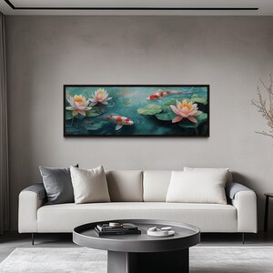 May include: A rectangular framed artwork depicting a serene pond scene with koi fish and water lilies. The painting features koi fish with red and white markings swimming among lily pads and blooming pink and yellow water lilies. The artwork is displayed above a white sofa.