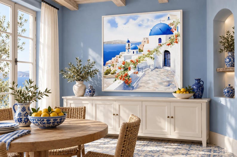 May include: A square framed wall art print depicting a Mediterranean coastal scene with white buildings, blue domes, and orange flowers. The artwork is displayed on a light blue wall above a long white wooden sideboard cabinet.