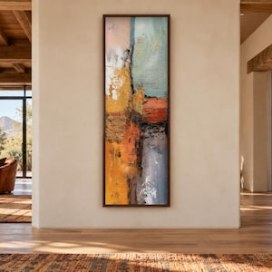 May include: A tall, rectangular abstract painting in a dark brown frame, featuring a vertical composition with textured layers of gold, burnt orange, deep red, muted blue, and grey tones, displayed on a plain, light-colored wall surface.