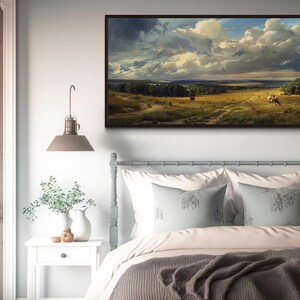 a serene bedroom scene with a large landscape painting hanging on the wall above a bed with white pillows and a gray blanket.