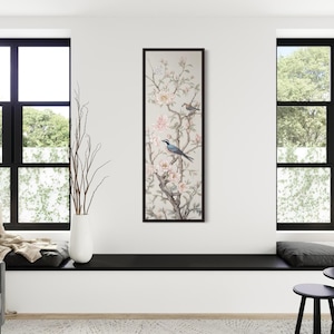 Pode incluir: Uma impressão de arte vertical emoldurada com uma ilustração detalhada de pássaros empoleirados em galhos floridos. A obra de arte tem um fundo neutro com tons suaves de rosa e cinza, e é exibida em uma moldura preta. A sala tem janelas com moldura preta e um sofá cinza.