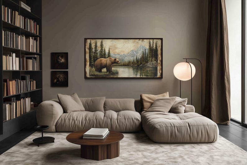 a cozy living room with a large painting of a bear in a forest scene hanging on the wall. The room features a beige sofa, a round wooden coffee table, and a floor lamp. The walls are painted in a neutral gray color, and the room is filled with bookshelves, creating a warm and inviting atmosphere.