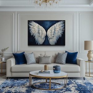 a luxurious living room with a large, striking painting of white wings on the wall. The room is furnished with a white sofa, a round coffee table, and a chandelier overhead. The overall decor has a modern and elegant style, with a blue and white color scheme.