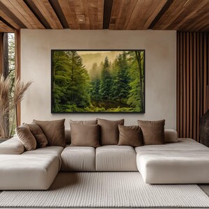 a modern living room with a large window overlooking a forest. The room has a white sofa with brown throw pillows, and a large framed landscape painting hanging on the wall above the sofa.