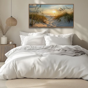 a serene bedroom scene with a large bed, white bedding, and a framed painting of a beach scene above it. The room has a minimalist and modern design, with a large window allowing natural light to fill the space.