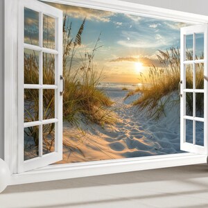 May include: A white window frame with open shutters reveals a beach scene at sunset. The view includes a sandy path, tall grasses, and the ocean under a colorful sky. Decorative vases and a sphere sit on a surface in front of the window.