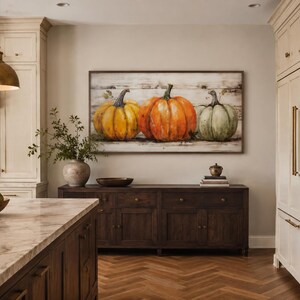 May include: A rectangular wall art piece featuring a painting of three pumpkins in yellow, orange, and green hues, set against a horizontal wood plank background. The artwork is framed in a dark wood border and displayed on a neutral-colored wall.