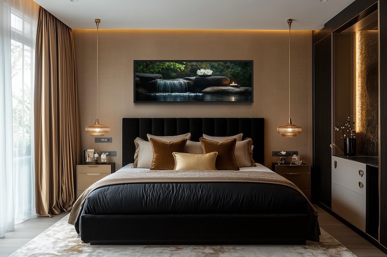 a luxurious bedroom with a large bed, dark headboard, and gold accents. The bed is adorned with a black comforter and gold throw pillows. Above the bed, there is a framed picture of a waterfall and flowers. The room features a large window with beige curtains, and the walls are painted in a light brown color. There are two pendant lights hanging above the bed, and a white dresser is visible on the right side of the room.