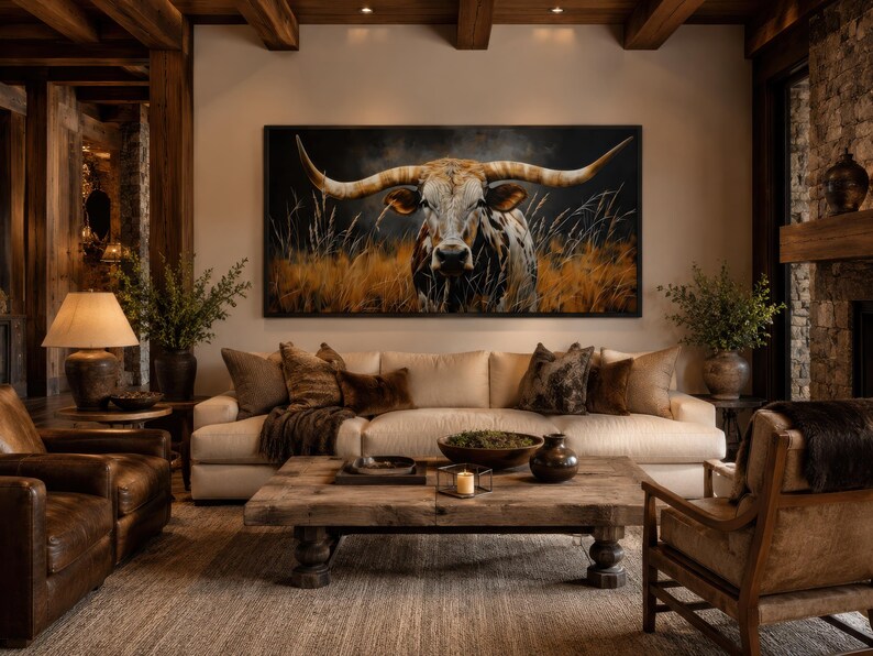 May include: A living room with a large painting of a longhorn bull above a cream-colored sofa. The room features a rustic wooden coffee table, leather armchairs, and a stone fireplace, creating a warm and inviting atmosphere. The decor includes throw pillows and decorative vases.