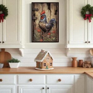 a kitchen with white cabinets, a wooden countertop, and a small gingerbread house on the counter. Above the countertop, there is a framed picture of a rooster. The kitchen also has Christmas decorations, including wreaths and a garland.