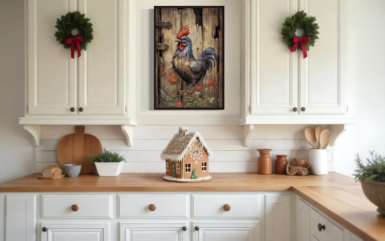 a kitchen with white cabinets, a wooden countertop, and a small gingerbread house on the counter. Above the countertop, there is a framed picture of a rooster. The kitchen also has Christmas decorations, including wreaths and a garland.