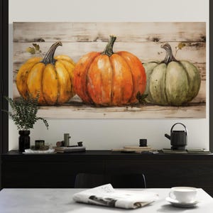 a dining room with a table and chairs, and a large painting of three pumpkins on the wall above the table.