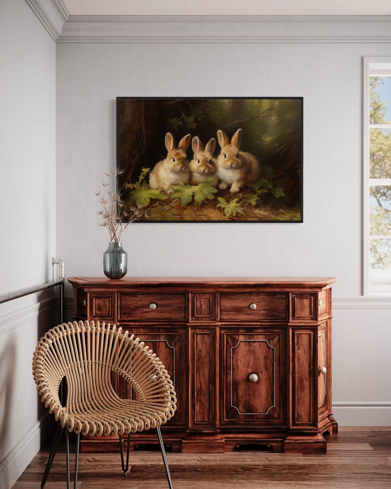 a painting of three rabbits on a wooden cabinet, with a woven chair in the foreground and a window in the background.
