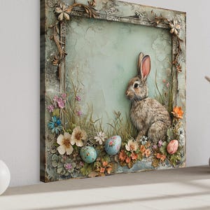 a large, ornate frame with a painting of a rabbit sitting in a grassy field surrounded by flowers and Easter eggs. The frame is placed on a shelf, and there are two white vases and a small white bowl on the shelf as well.