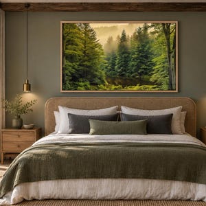May include: A rectangular framed wall art print featuring a misty forest landscape with dense green pine trees and soft golden light, displayed above a bed with a textured olive green coverlet, white linens, and dark gray accent pillows.