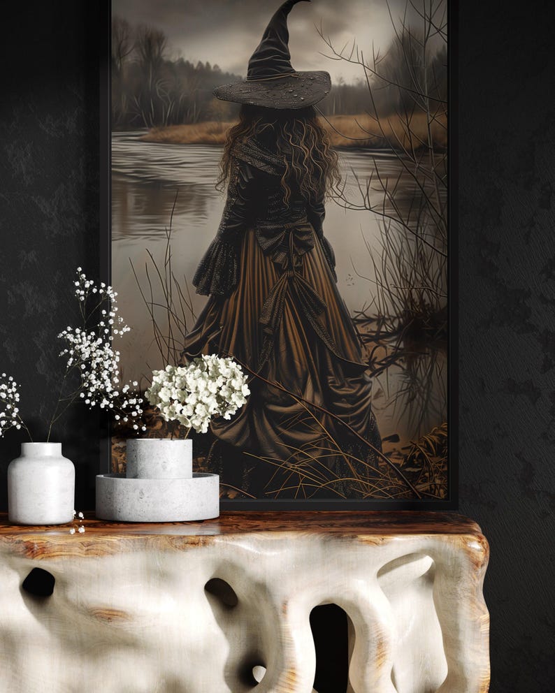 a woman in a long black dress with a pointed hat, standing in front of a painting of a woman in a similar dress, with a body of water and trees in the background.