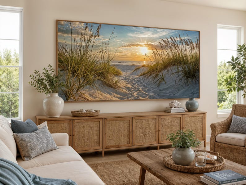May include: A large rectangular wall art print featuring a sunset over a sandy beach with tall dune grasses in the foreground. The scene depicts a golden sun low on the horizon, casting light over the ocean waves and a path through the dunes.
