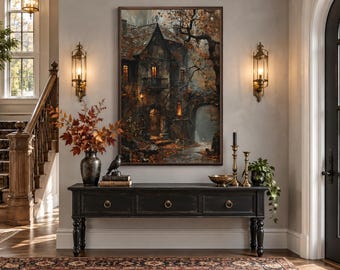 Puede incluir: Una impresión artística rectangular enmarcada que representa una cabaña de piedra oscura y atmosférica en un bosque otoñal, con ventanas de luz cálida, árboles desnudos y hojas caídas, exhibida sobre una mesa consola de madera negra.