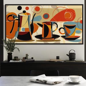 May include: Abstract art print featuring coffee pots, cups, and saucers in orange, black, and blue. The artwork is framed in black and hangs above a black cabinet. A small black teapot and a vase with greenery are also visible.