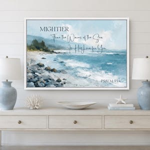 May include: A rectangular wall art print in a white frame featuring a coastal landscape painting with blue ocean waves, a rocky shoreline, and the text: MIGHTIER Than the Waves of the Sea Is His Love for You PSALM 93:4 in dark blue lettering.