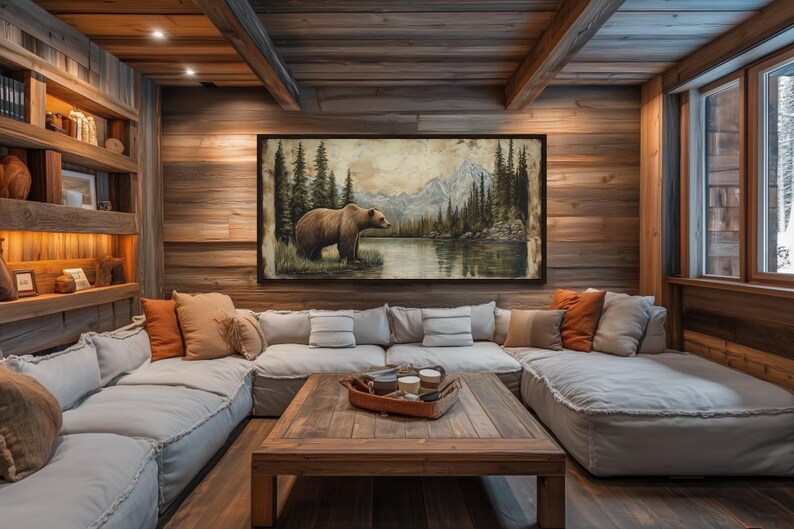 a cozy living room with a large painting of a bear in a forest scene hanging on the wall. The room has a rustic, cabin-like atmosphere with wooden walls and ceiling, and a comfortable couch and coffee table arranged around the space.