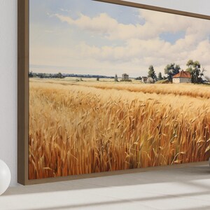 a large painting of a golden wheat field with a house in the distance, set against a blue sky with clouds. The painting is framed and displayed on a wall, with two white vases placed on either side of it.