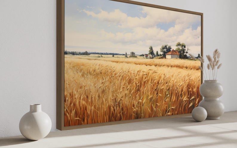 a large painting of a golden wheat field with a house in the distance, set against a blue sky with clouds. The painting is framed and displayed on a wall, with two white vases placed on either side of it.