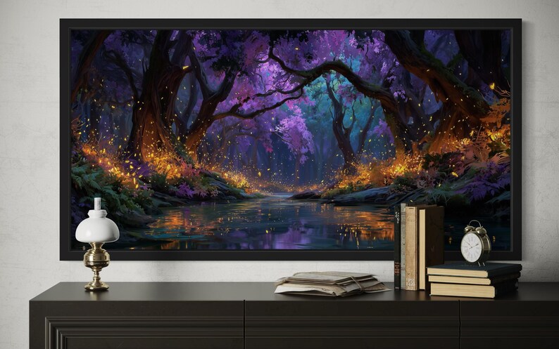Op de afbeelding: Een ingelijste kunstdruk die een mystieke bossc&egrave;ne met een rivier afbeeldt. Het kunstwerk heeft een levendig kleurenpalet van paars, blauw en goud, met gedetailleerde bomen en gloeiende deeltjes. De print wordt getoond op een zwarte kast.
